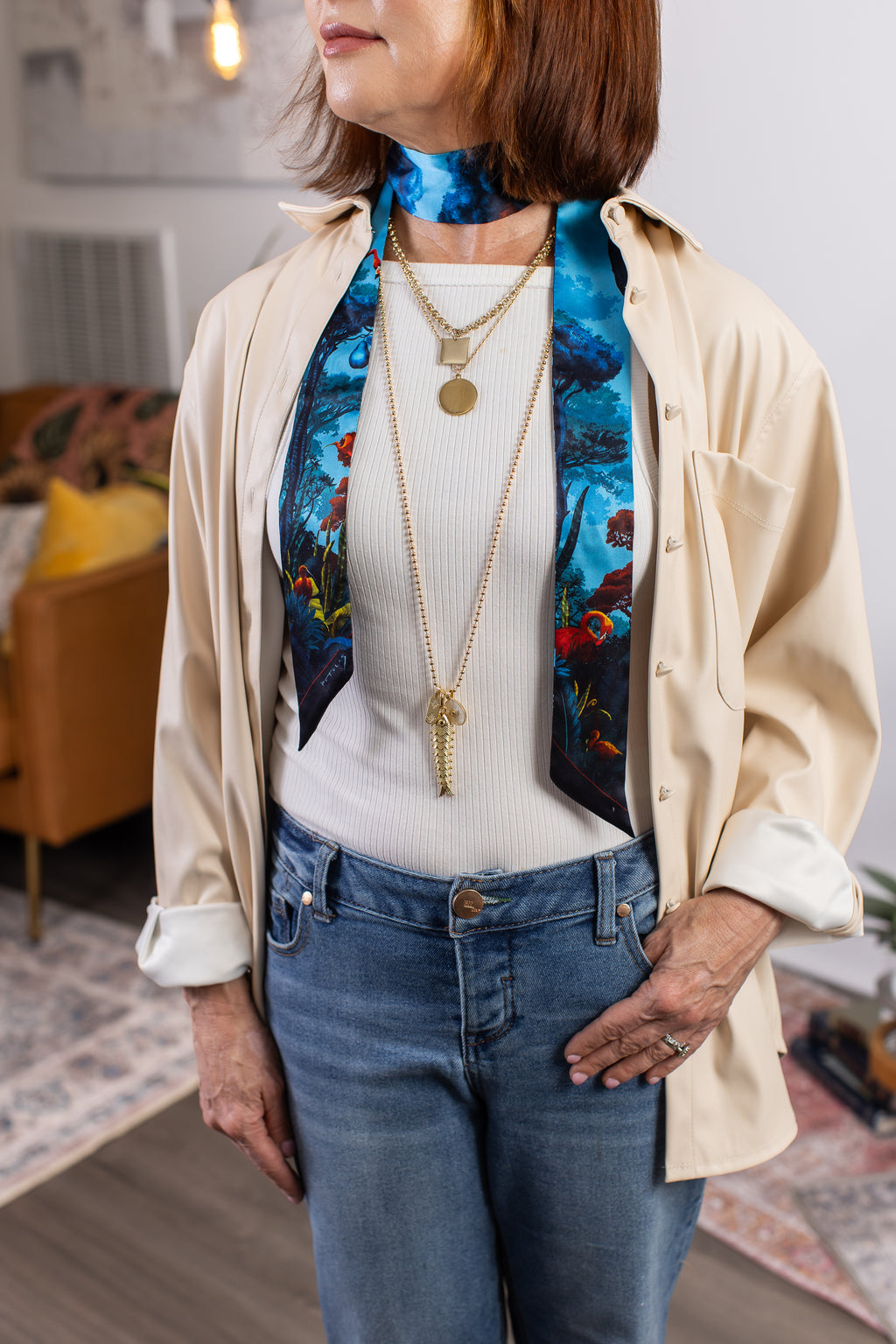 Woman wearing a colorful scarf, layered necklaces, and a beige shirt with a white top.