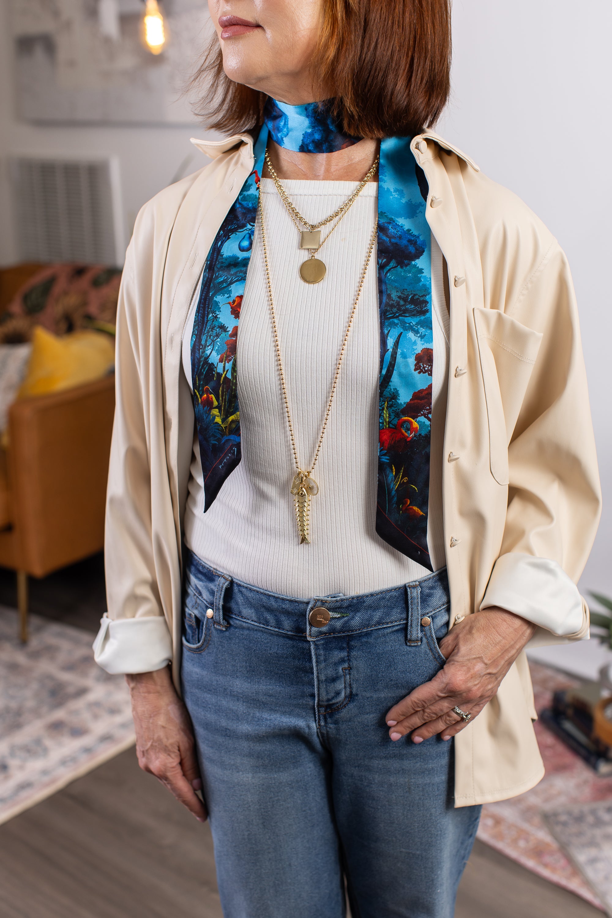 Woman wearing a colorful scarf, layered necklaces, and a beige shirt with a white top.